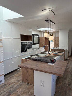 Cocina moderna con armarios blancos, encimera de madera e iluminación colgante.