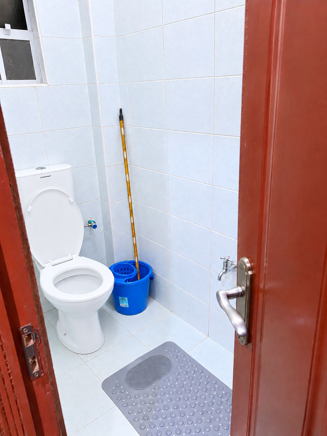 Une petite salle de bain avec des toilettes, une serpillière et un seau bleu.