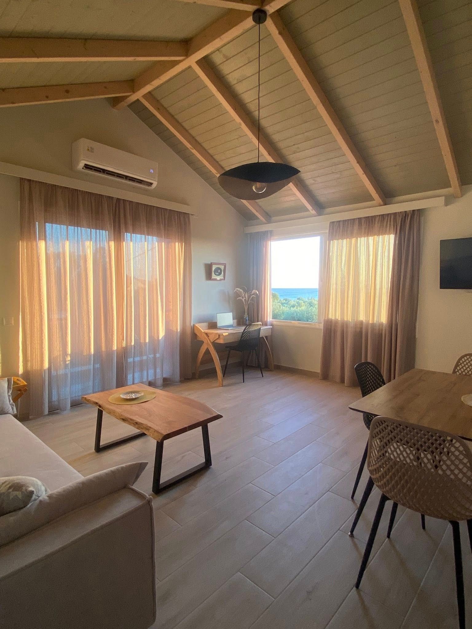 A spacious living area with a wooden ceiling, a dining table, and a view of the sea.