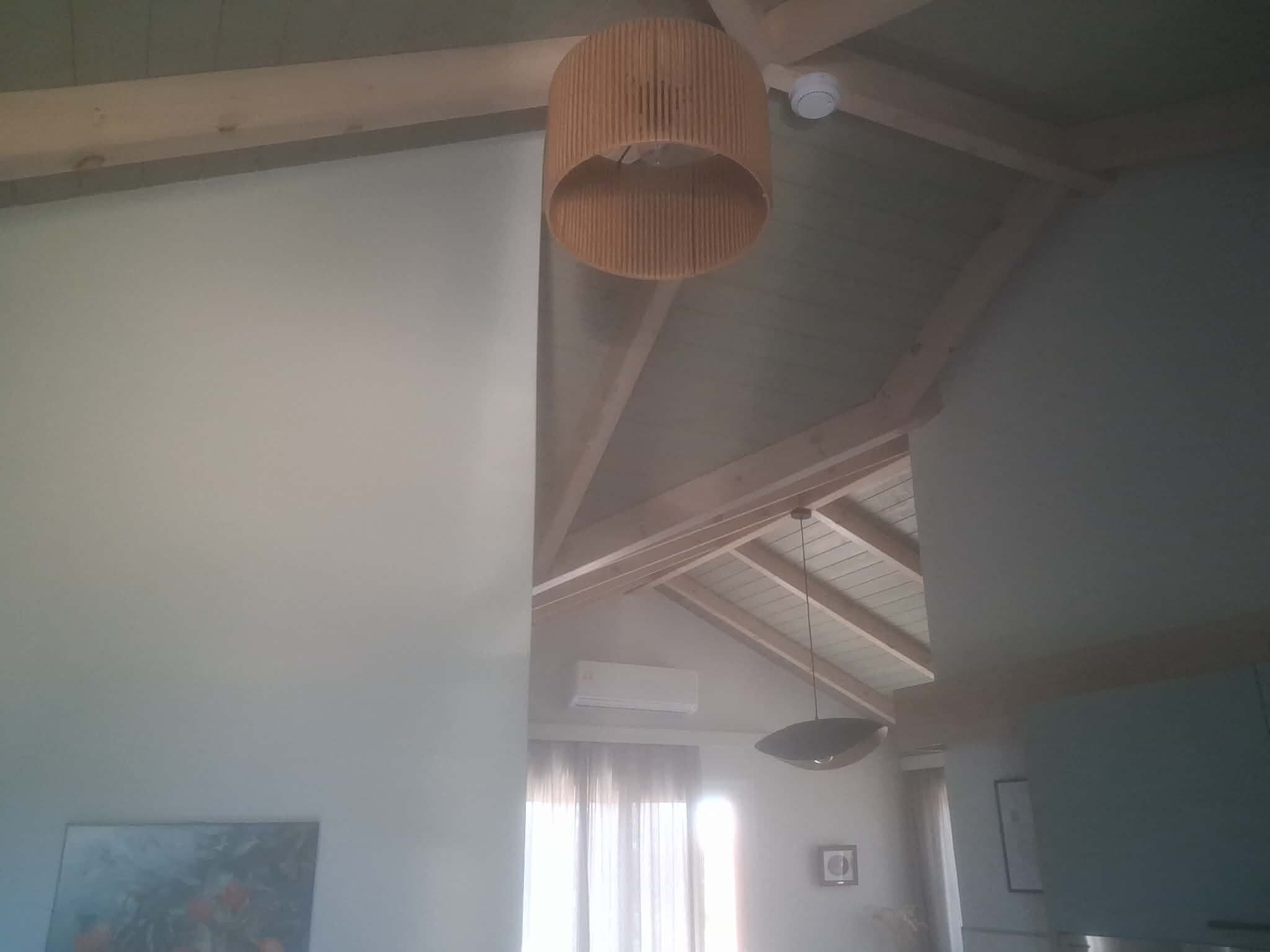 A room with a high ceiling, wooden beams, a hanging light fixture, and a window with curtains.