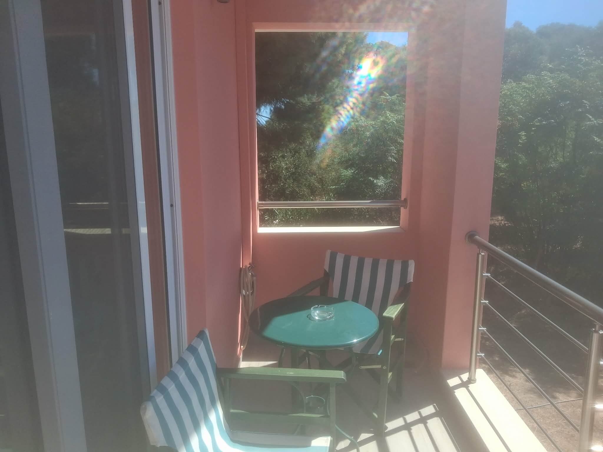 Un balcon avec une table et des chaises, une vue sur les arbres et une porte.