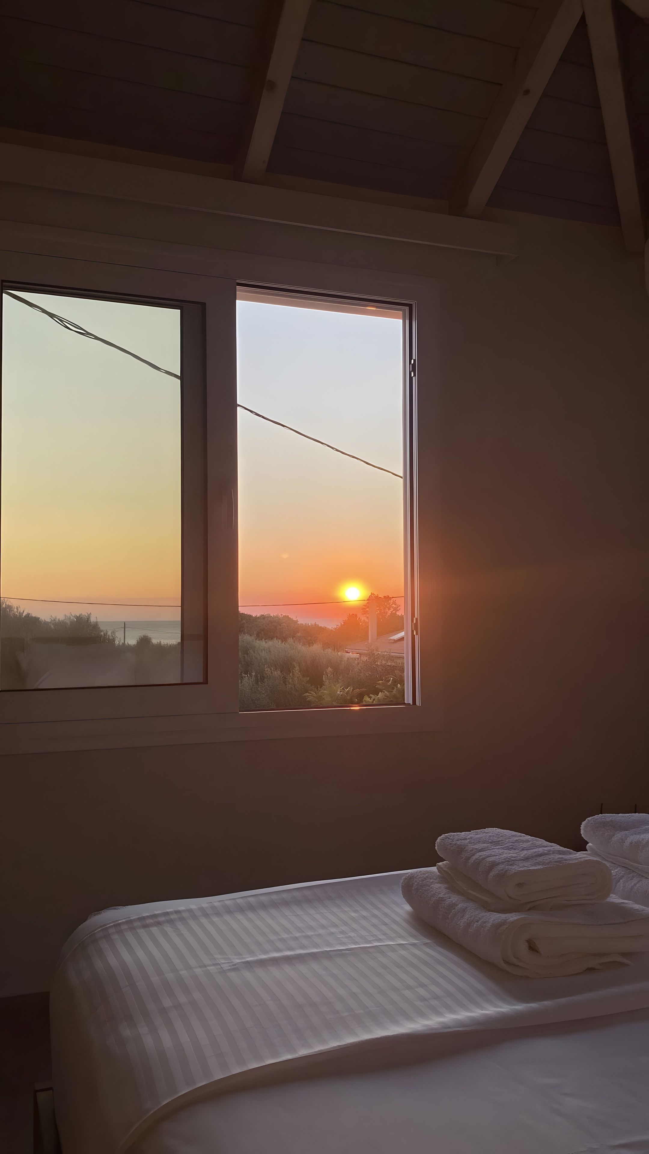 Een slaapkamer met een bed, een raam met uitzicht op de zonsondergang en een wandplank.