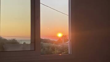 Een slaapkamer met een bed, een raam met uitzicht op de zonsondergang en een wandplank.