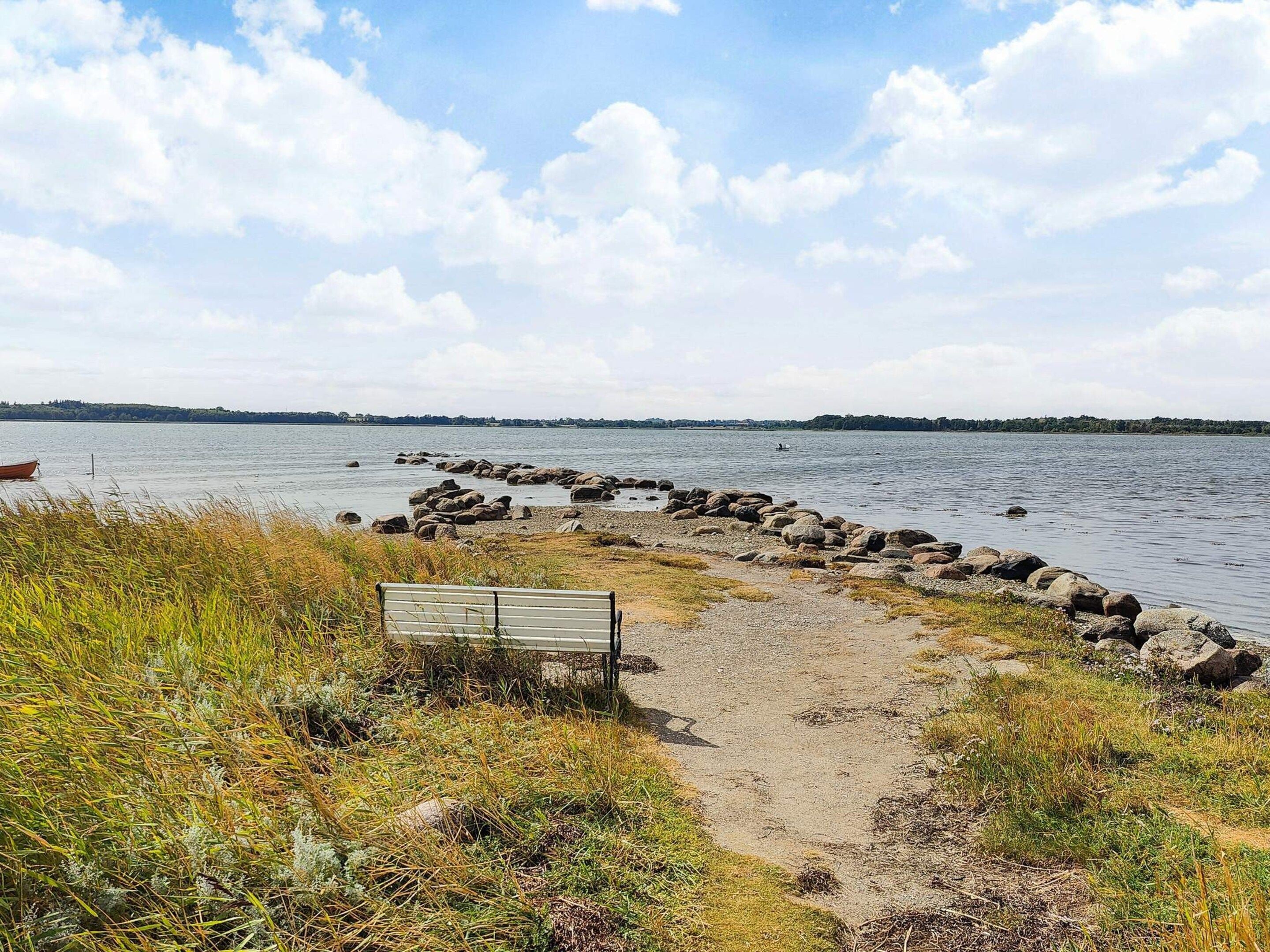 A pathway leading to a body of water with a bench and a row of rocks along the shore.