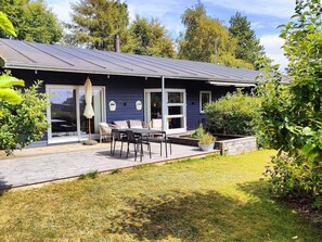 Una casa moderna con un patio, mobiliario de exterior y un jardín.