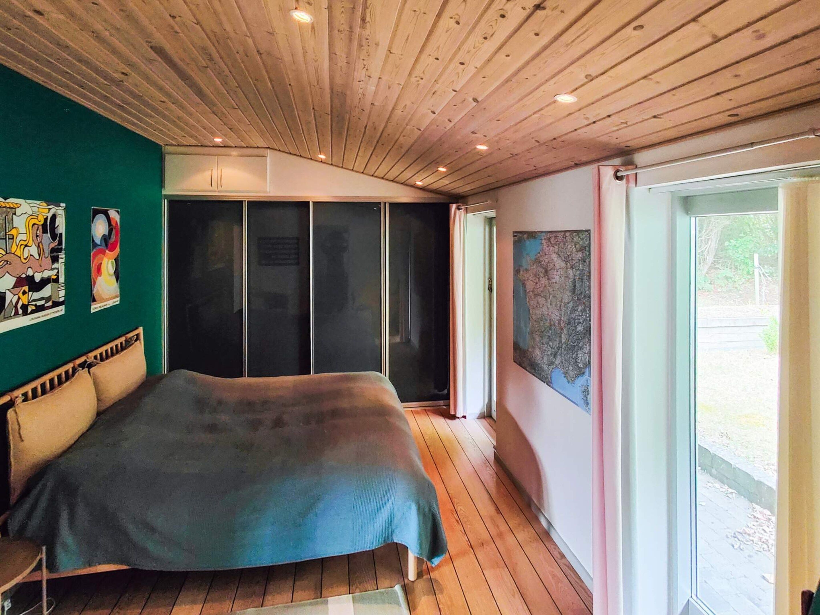 A bedroom with a bed, a wooden ceiling, a green wall, and a window.