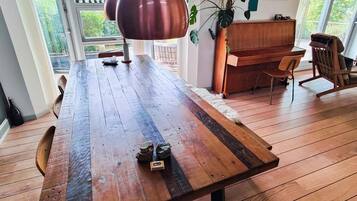 A wooden dining table with a rustic finish, a hanging pendant light, and a piano in the background.