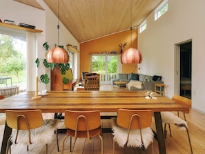 A modern living space with a wooden dining table, chairs, a sofa, and a large window offering a view of greenery. - 7 Person Holiday Home in Oro (Orø)