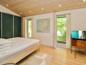 A bedroom with a bed, a desk, a map on the wall, and a view of greenery outside. - 7 Person Holiday Home in Oro (Orø)