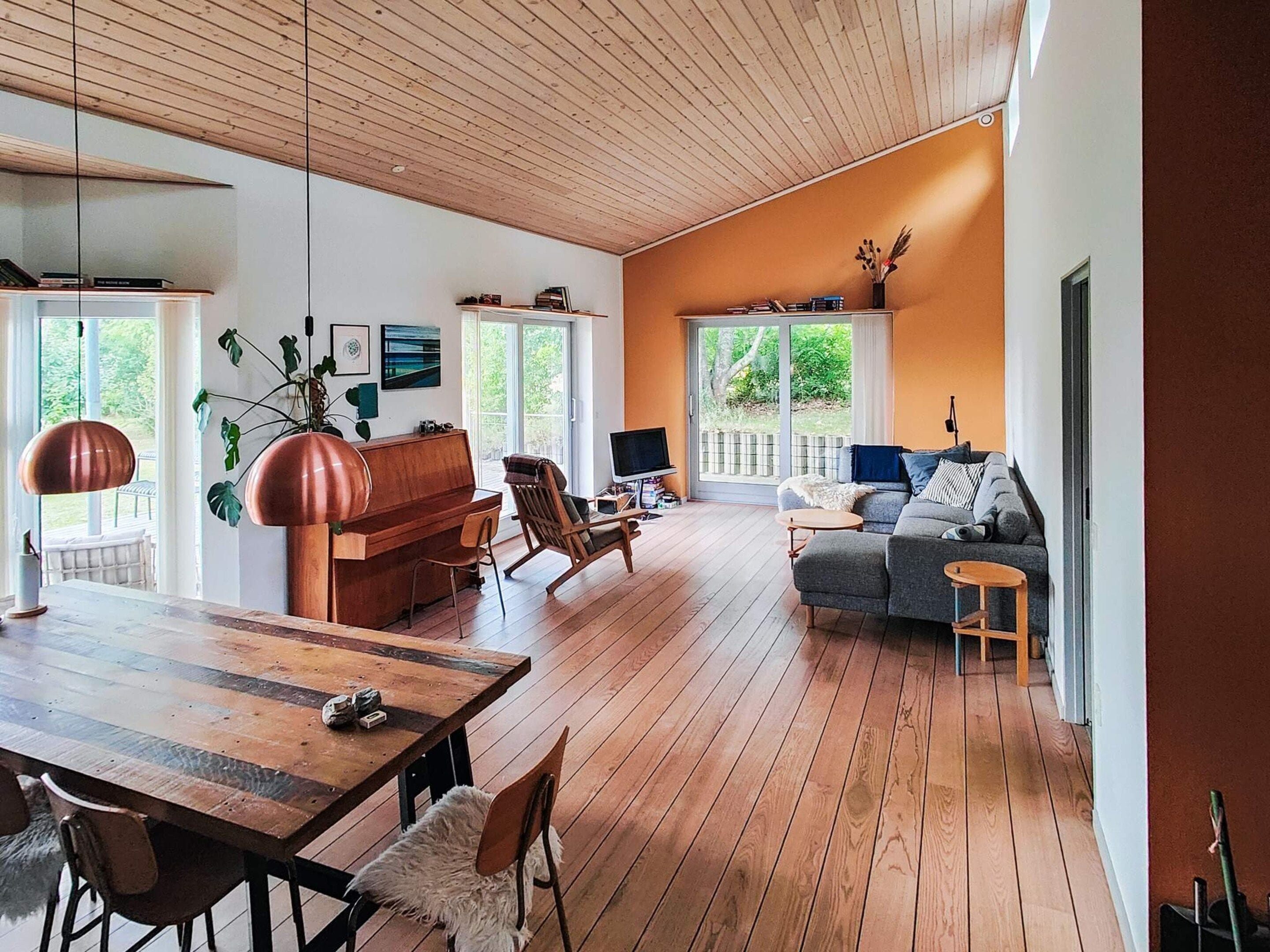 A spacious living room with a wooden floor, a piano, a sofa, and a dining area with a table and chairs.