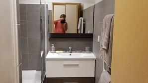 A modern bathroom with a bathtub, a sink with a mirror above it, and a towel rack. - Apartment 'Les Orangers' with Private Garden, Wi-Fi and Air Conditioning (Cannes)