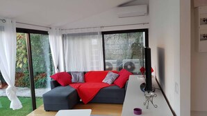 A modern living room with a grey sofa, red and grey cushions, a white coffee table, and a small side table with a purple object. - Apartment 'Les Orangers' with Private Garden, Wi-Fi and Air Conditioning (Cannes)