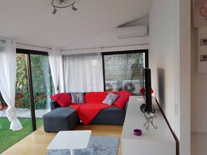 A modern living room with a grey sofa, red and grey cushions, a white coffee table, and a small side table with a purple object. - Apartment 'Les Orangers' with Private Garden, Wi-Fi and Air Conditioning (Cannes)