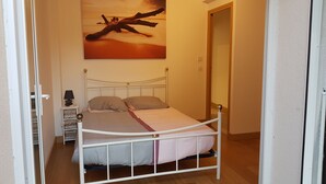 A bedroom with a bed, bedside table, lamp, and a painting on the wall. - Apartment 'Les Orangers' with Private Garden, Wi-Fi and Air Conditioning (Cannes)