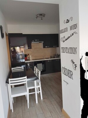 A modern kitchen with black cabinets, a wooden countertop, and a dining area with white chairs. - Apartment 'Les Orangers' with Private Garden, Wi-Fi and Air Conditioning (Cannes)