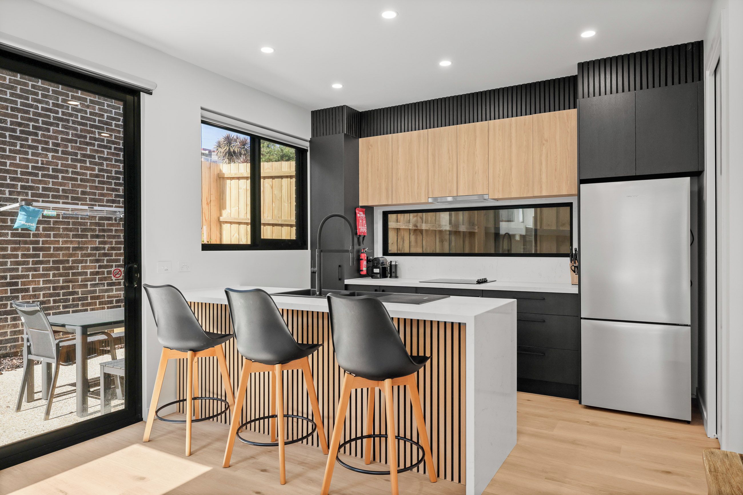 A modern kitchen with a central island, black and wooden cabinetry, and a stainless steel refrigerator.