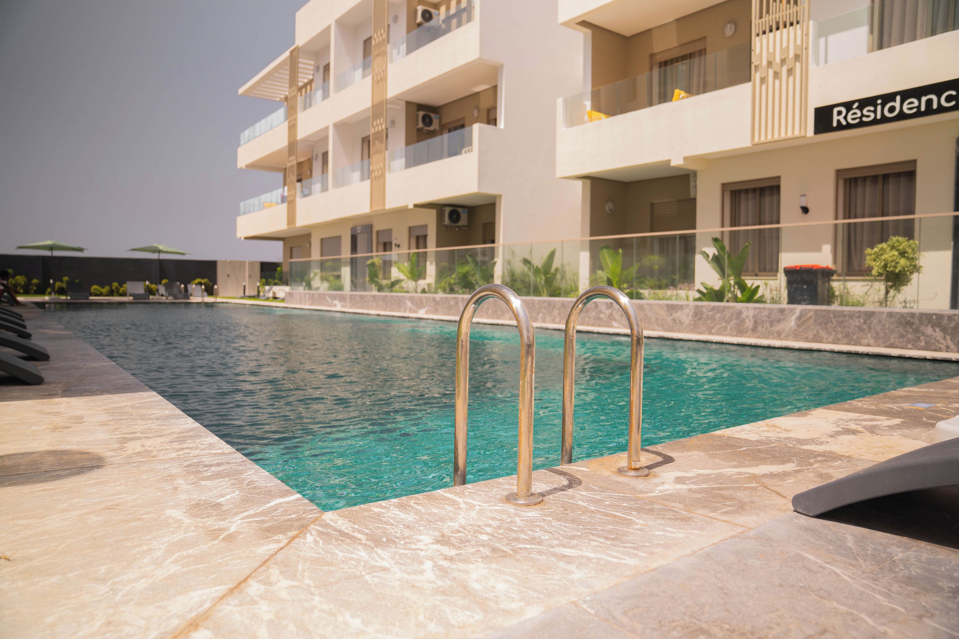 A swimming pool with metal railings, surrounded by a tiled deck.