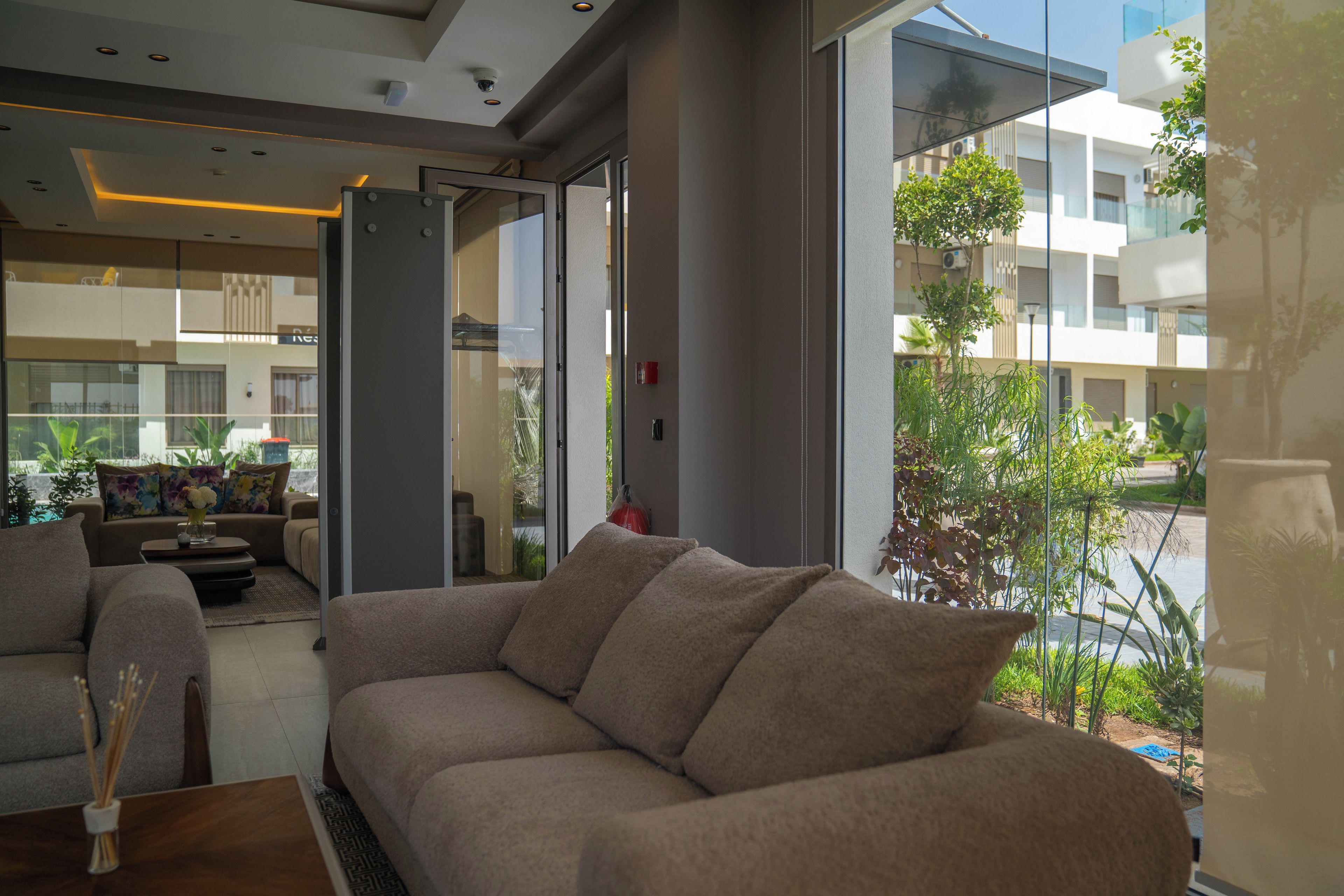 A modern living room with a sofa, a coffee table, and a view of a building through large windows.