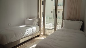 Quarto de hotel com duas camas, uma mesinha e vista para a varanda.