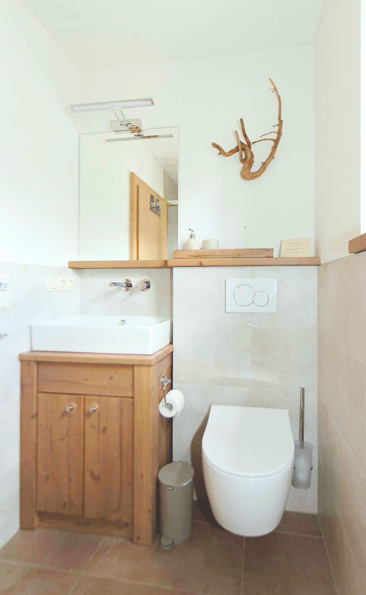 Ein Badezimmer mit einem Holzkosmetikschrank, einem weißen Waschbecken, einer Toilette und einem an der Wand befestigten Spiegel.