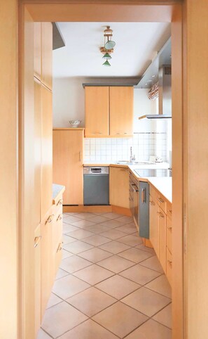 A kitchen with wooden cabinets, a dishwasher, and a tiled floor. - Lacus Apartment by Loewenherz (Krün)