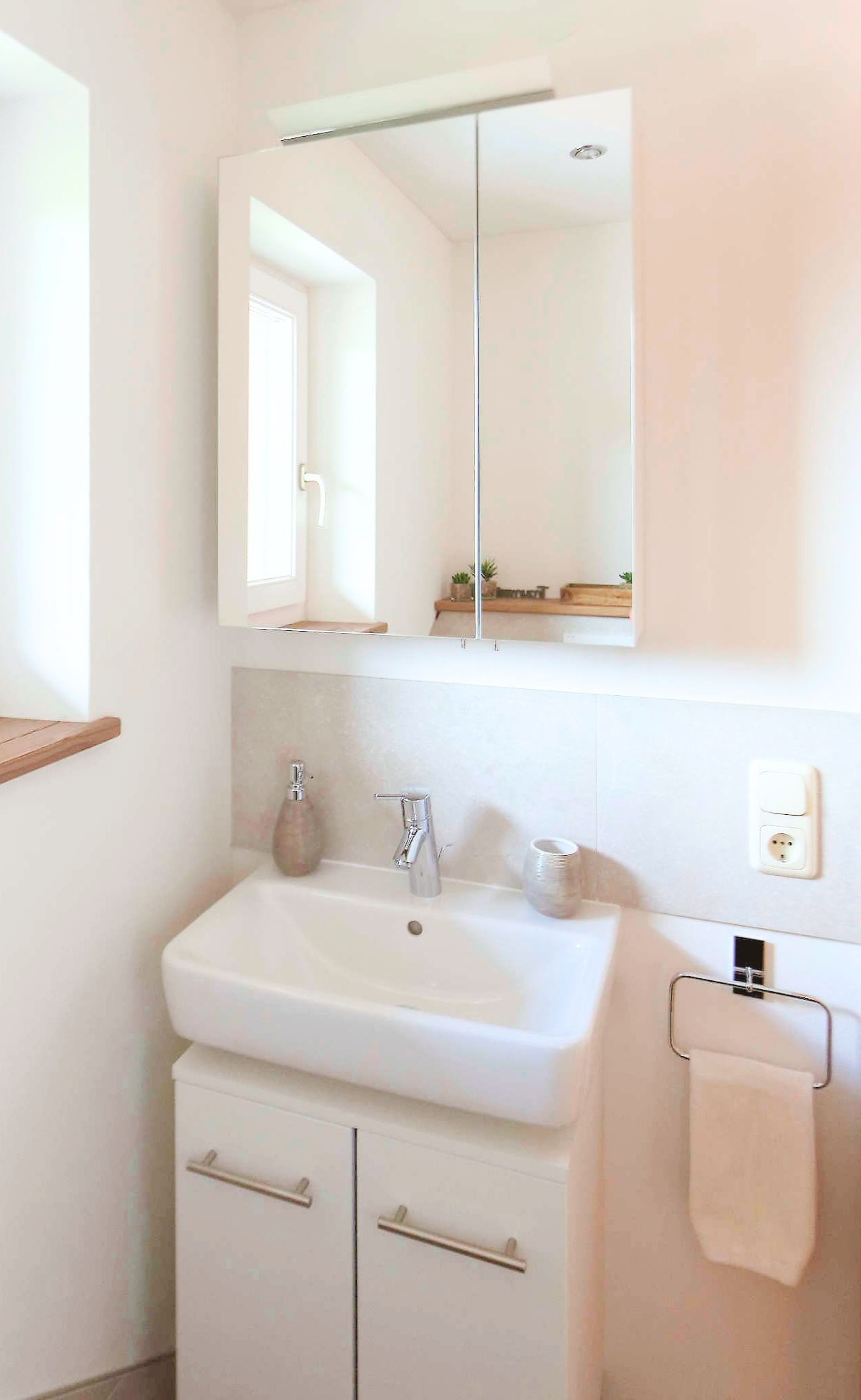 A bathroom with a white sink, a mirror, a towel rack, and a small shelf.
