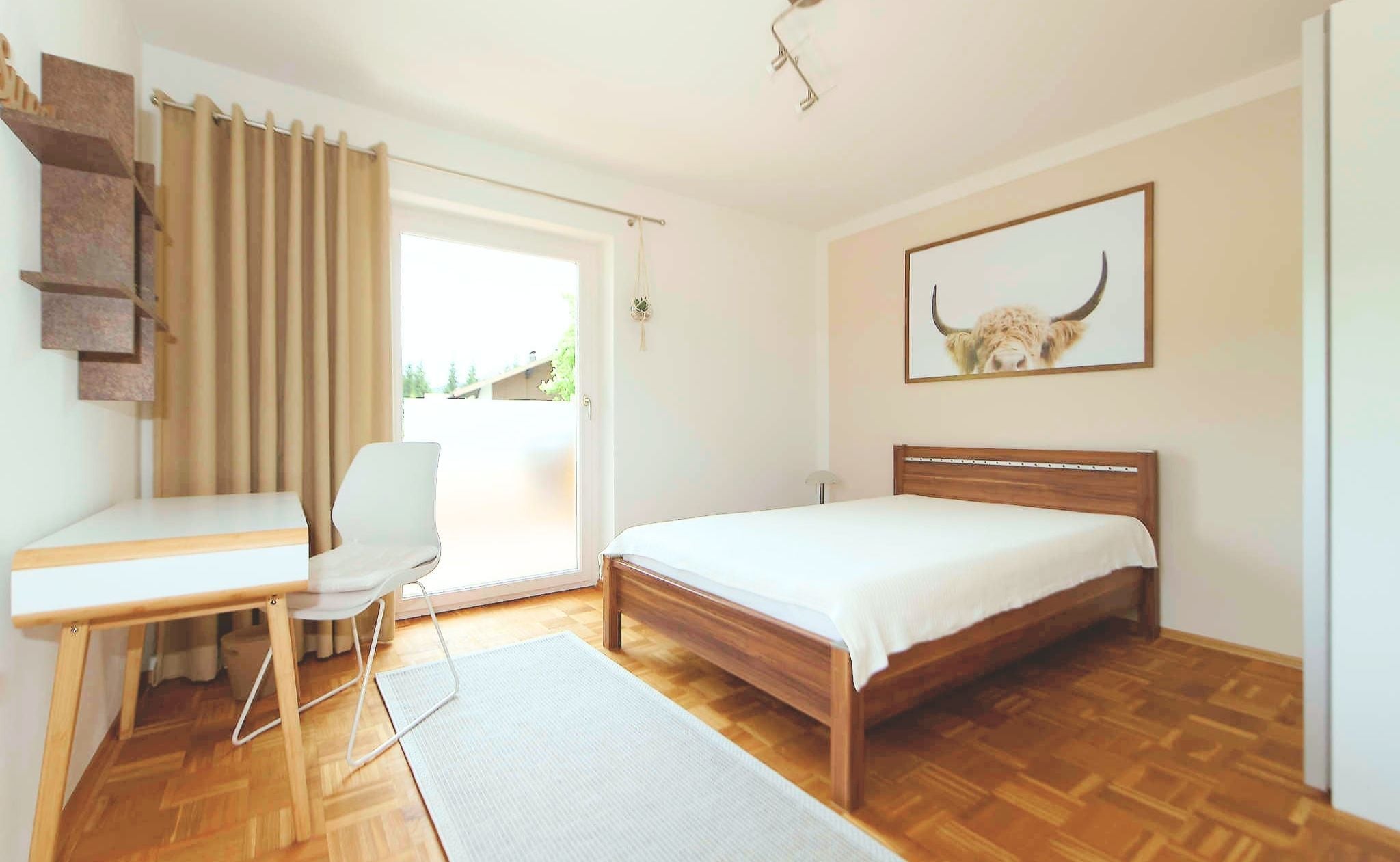 A bedroom with a bed, a desk, a chair, and a window with curtains.