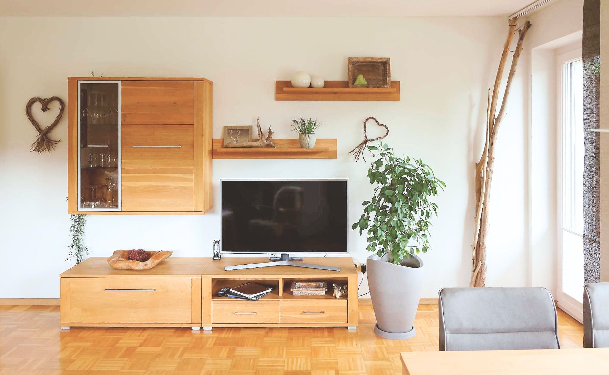 Ein Wohnzimmer mit Holzschrank, Flachbildfernseher, Topfpflanze und grauem Sofa.