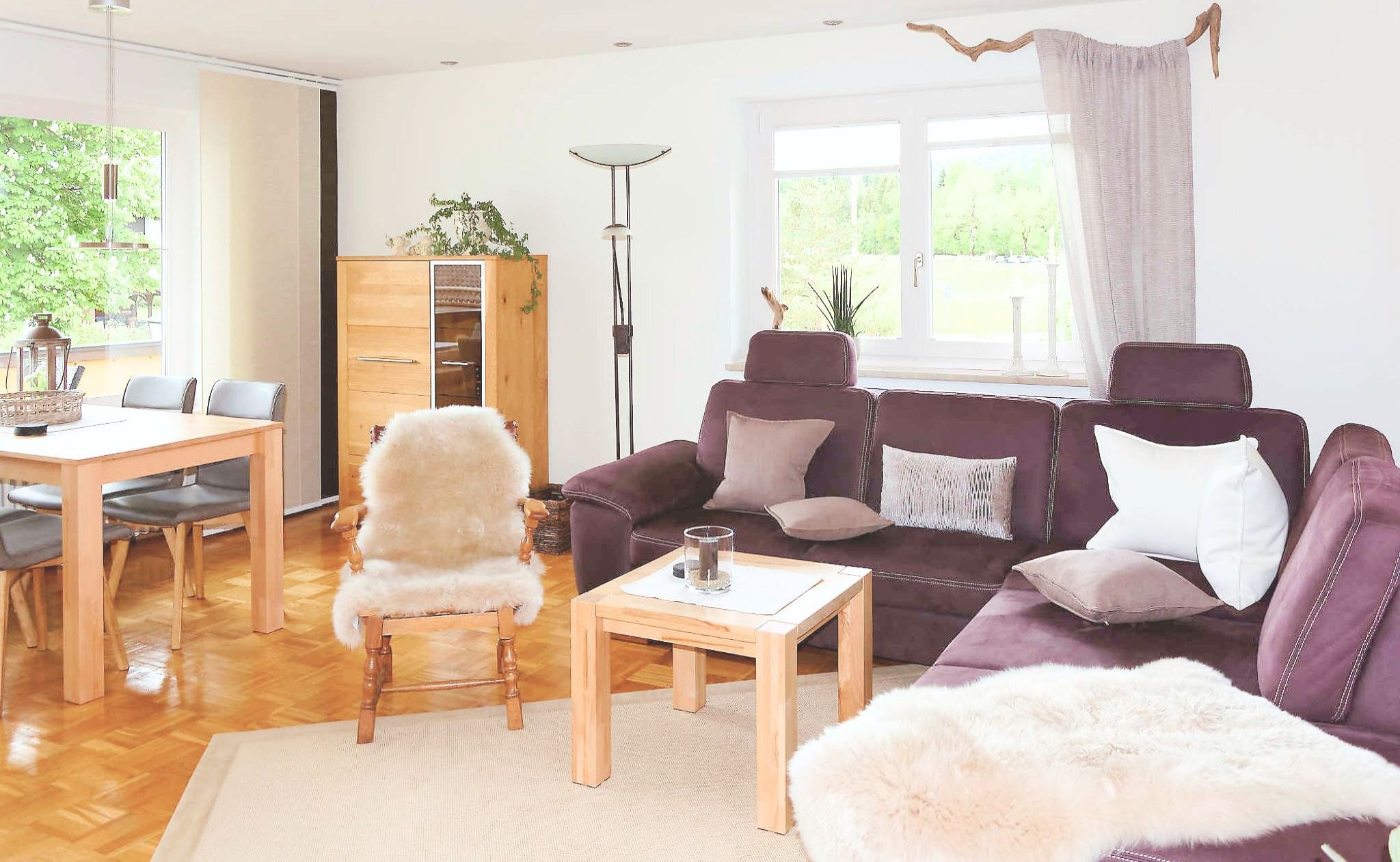 A living room with a wooden dining table, a purple sofa, a fluffy chair, and a floor lamp.