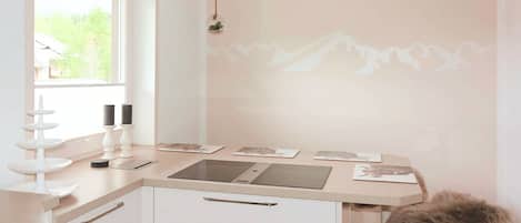Une cuisine moderne avec une fenêtre, un luminaire fixé au mur et un plan de travail sur lequel se trouvent un ordinateur portable et des documents.