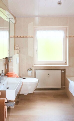 Ein Badezimmer mit einem Doppelwaschbecken, einer Toilette, einem Fenster mit Vorhang und einer Heizung.