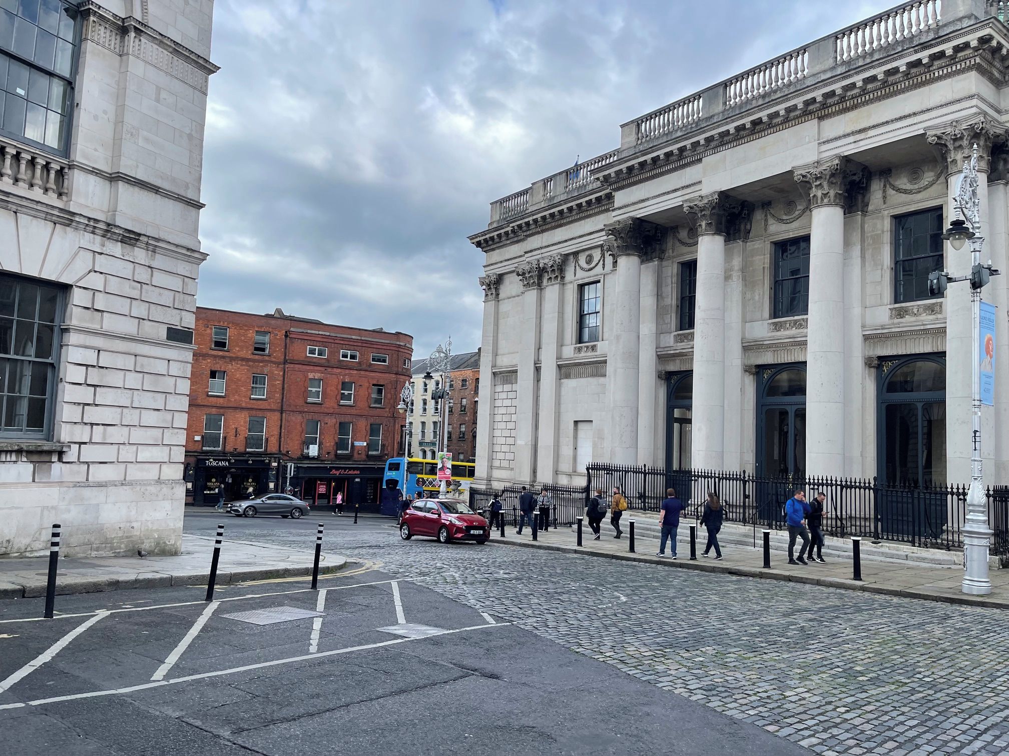 A cobblestone street with historic buildings, a double-decker bus, and pedestrians.