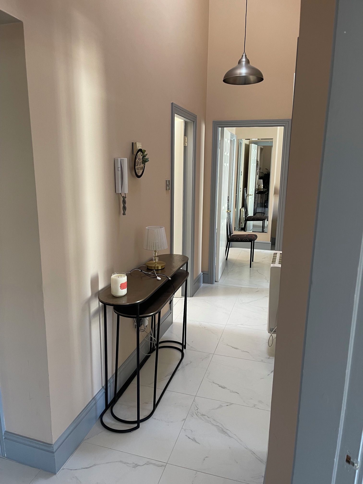 A hallway with a table, chair, pendant light, and a door leading to another room.