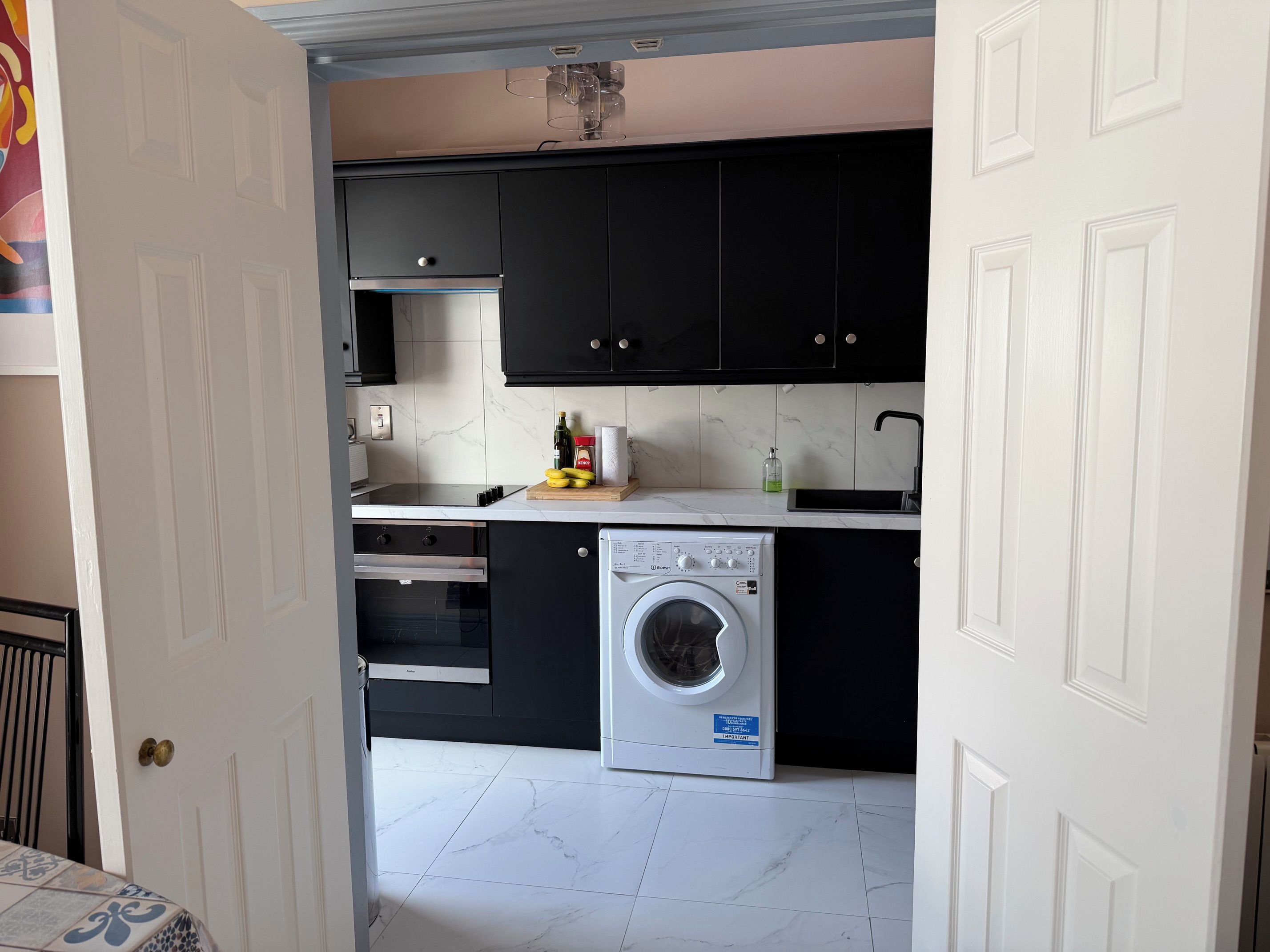 Une cuisine compacte avec des meubles noirs, un four à micro-ondes encastré, un évier et un lave-linge à chargement frontal.