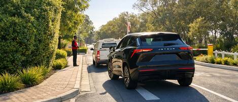 A road with a 'VISITOR' marking, a white vehicle, and a person standing by the curb.