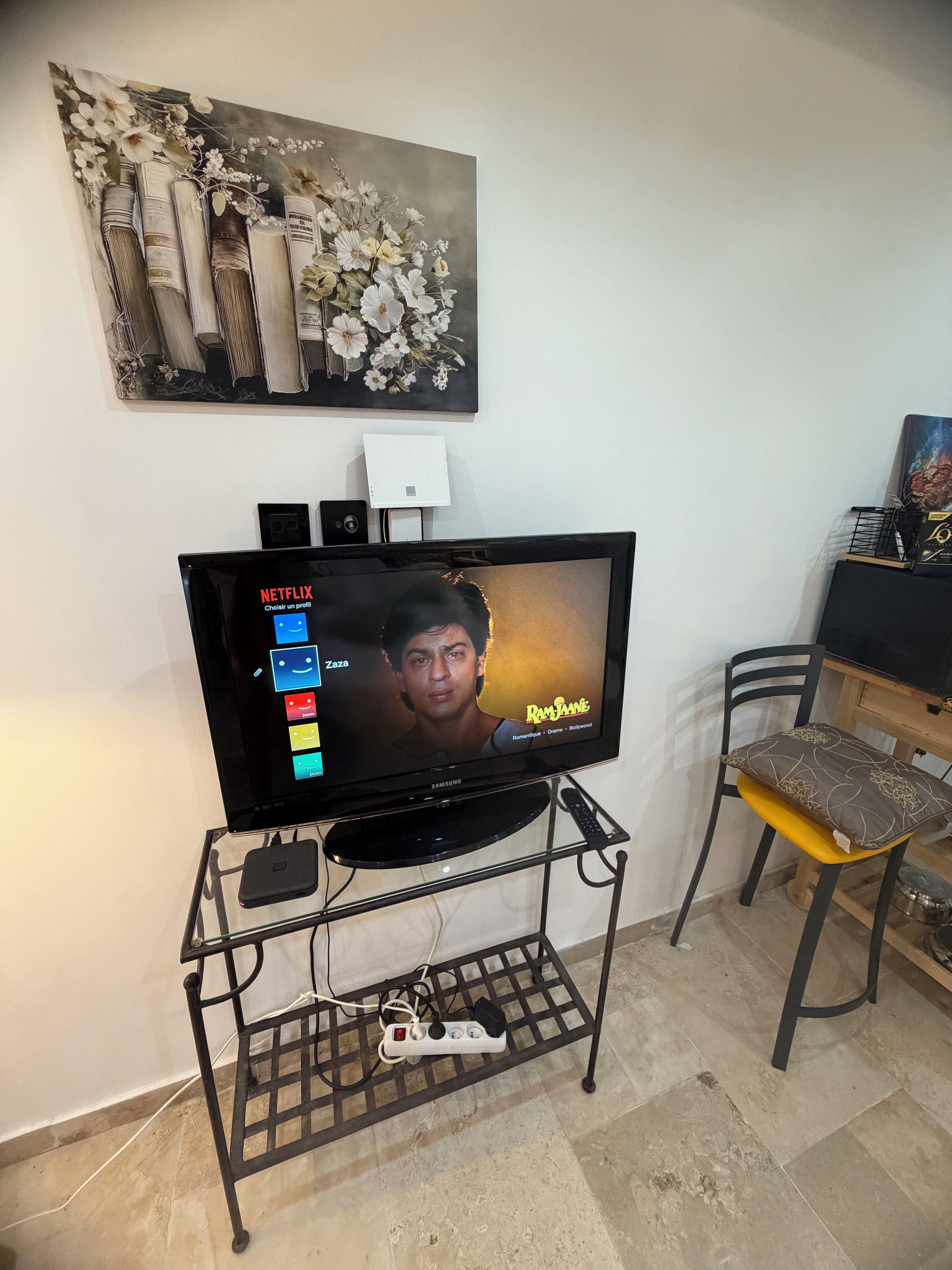 Un téléviseur posé sur un meuble, avec l’interface Netflix affichée à l’écran, un haut-parleur et une multiprise.