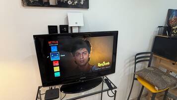 Un téléviseur posé sur un meuble, avec l’interface Netflix affichée à l’écran, un haut-parleur et une multiprise.