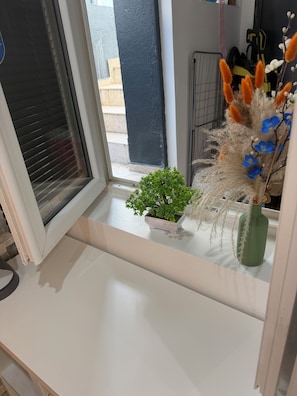 A window with a small potted plant and decorative flowers on a white ledge.