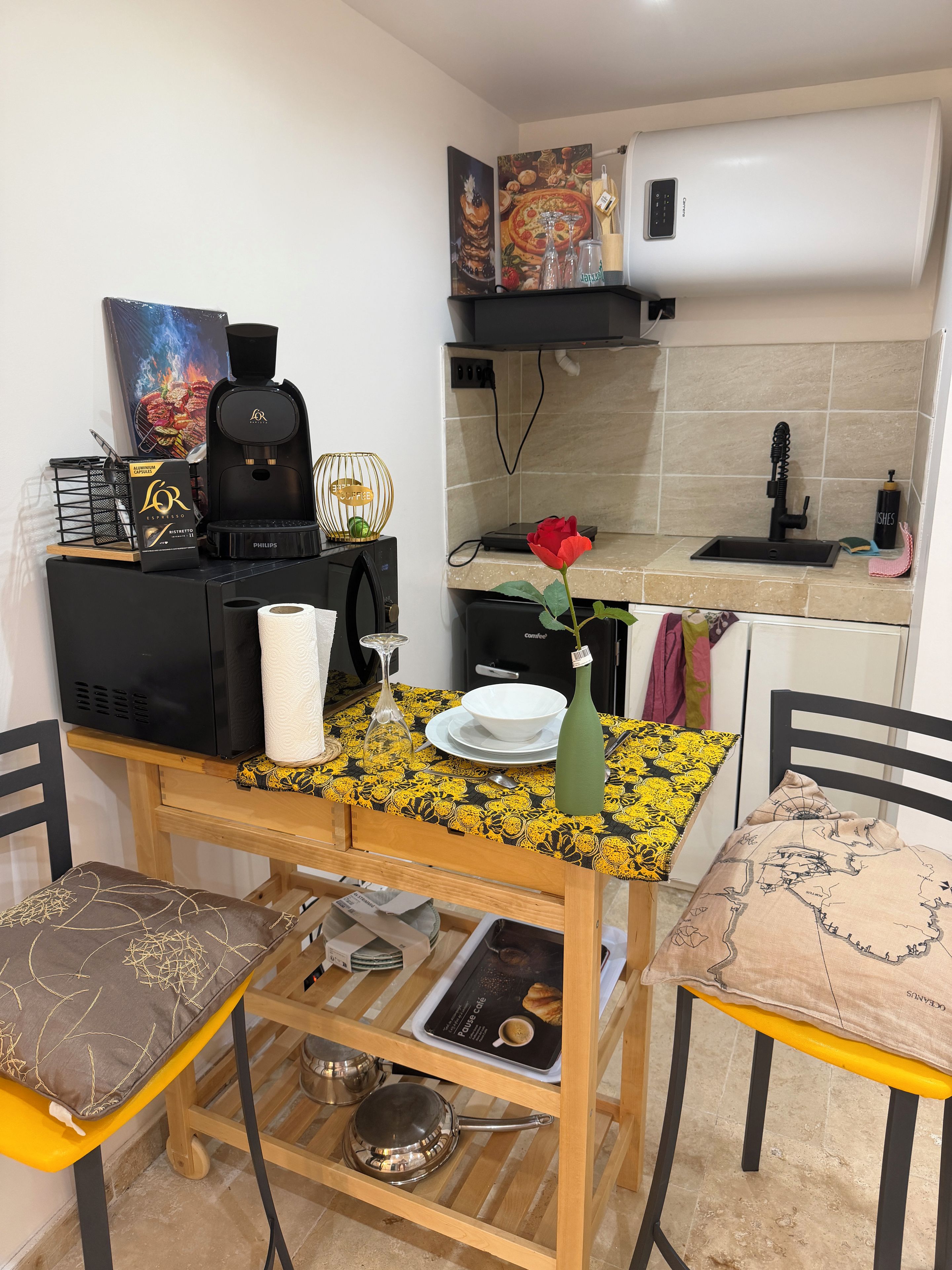 Una cocina compacta con cafetera, lavamanos y comedor con mesa y sillas.