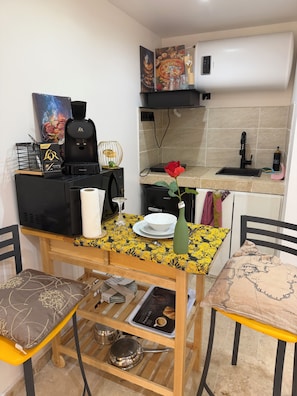 A compact kitchen with a coffee machine, a sink, and a dining area with a table and chairs.