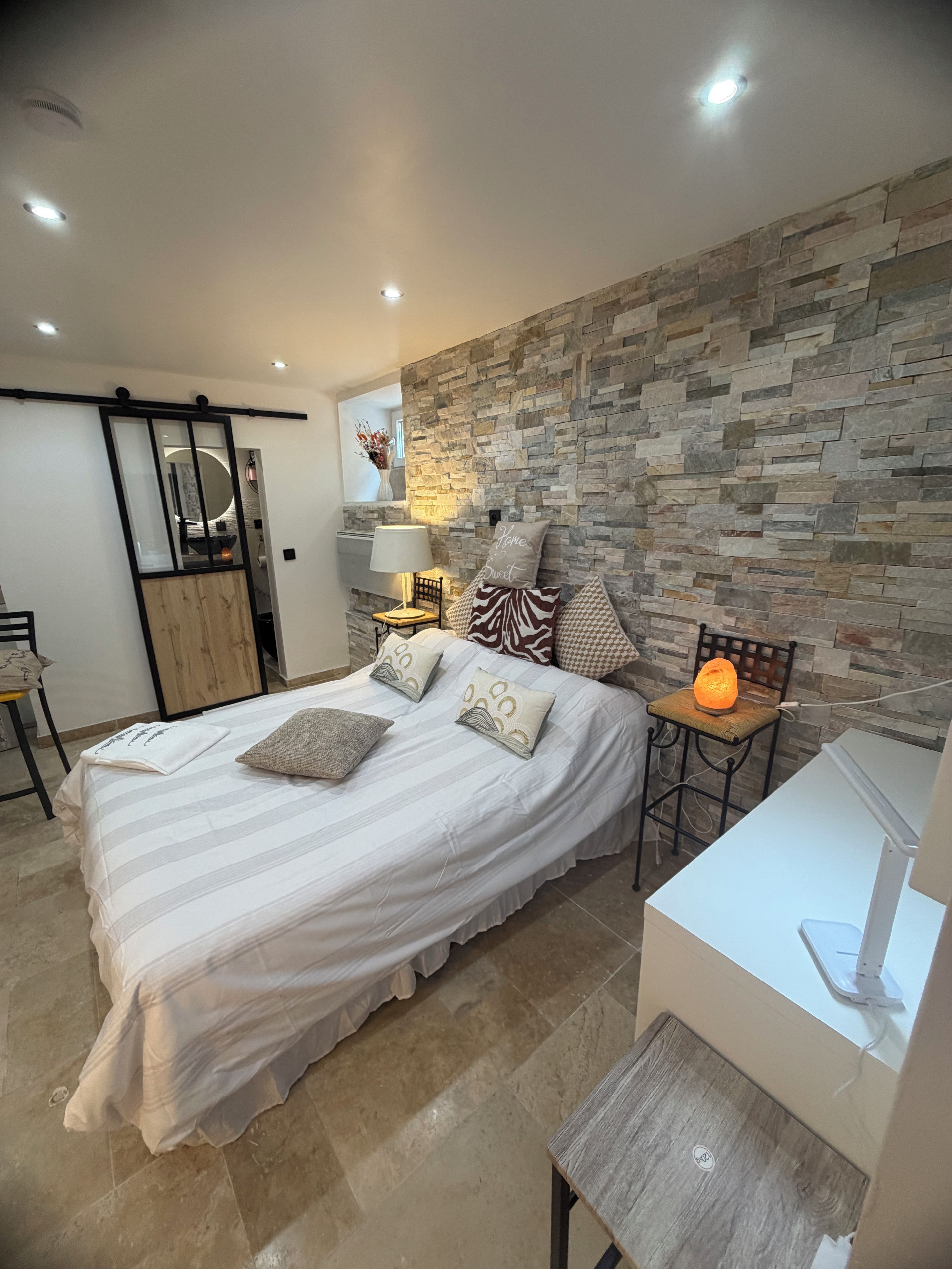 Un dormitorio con una cama, un escritorio, una silla y una pared de piedra.