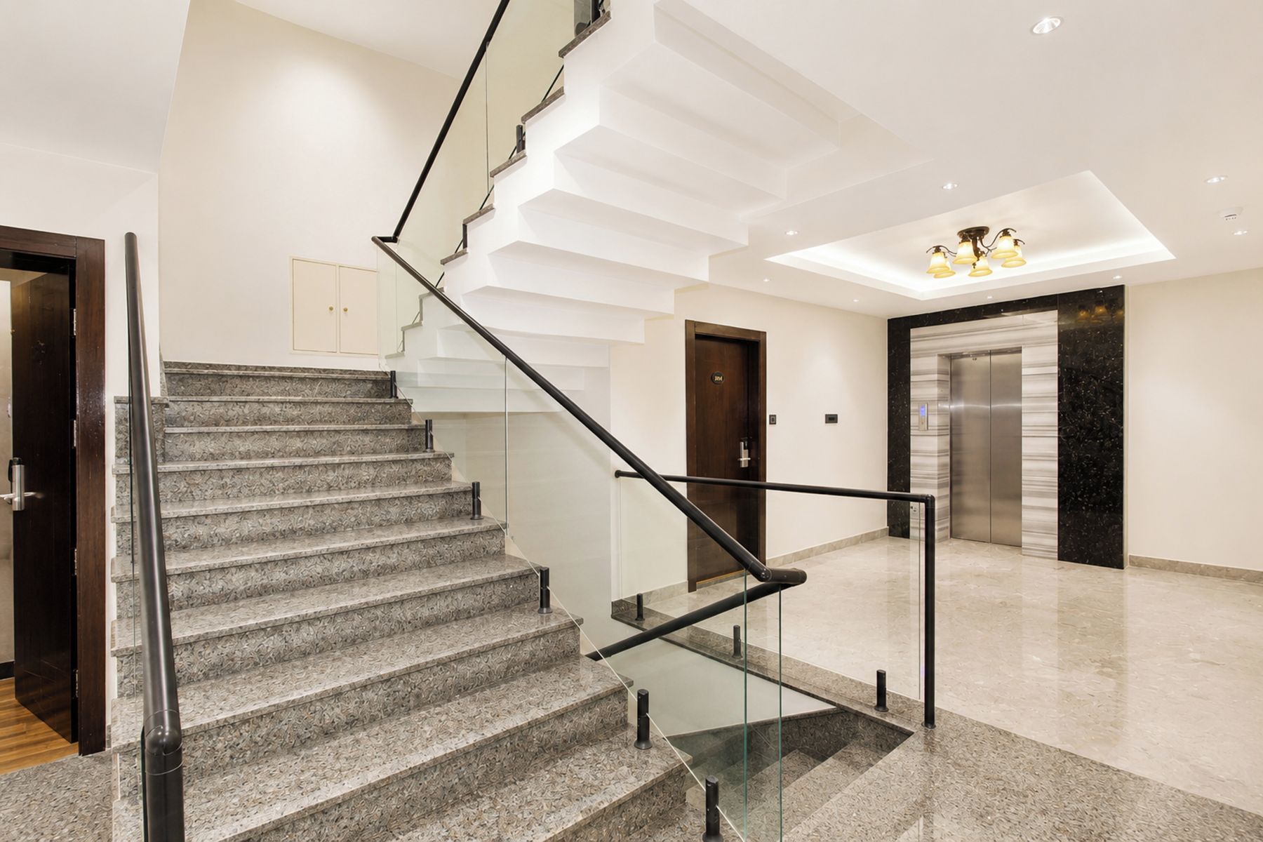 A modern interior with a marble staircase, a glass railing, and a sleek elevator.