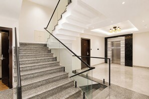 A modern interior with a marble staircase, a glass railing, and a sleek elevator. - Hotel Greeno's (Gangtok)