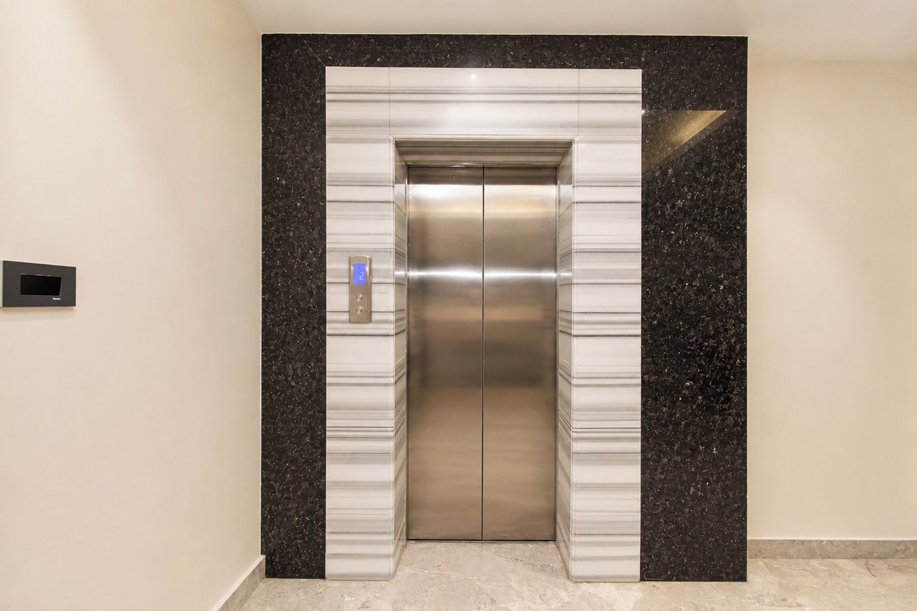 An elevator with a digital display and a control panel, surrounded by walls with a speckled pattern.