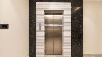 An elevator with a digital display and a control panel, surrounded by walls with a speckled pattern.
