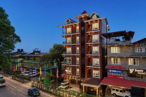 A multi-story hotel with a prominent central tower, a ground-level restaurant, and a visible HDB Financial Services sign. - Hotel Greeno's (Gangtok)