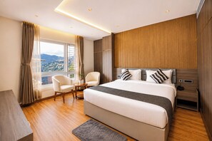 A modern hotel room with a large bed, two armchairs, a wooden floor, and a view of a cityscape. - Hotel Greeno's (Gangtok)