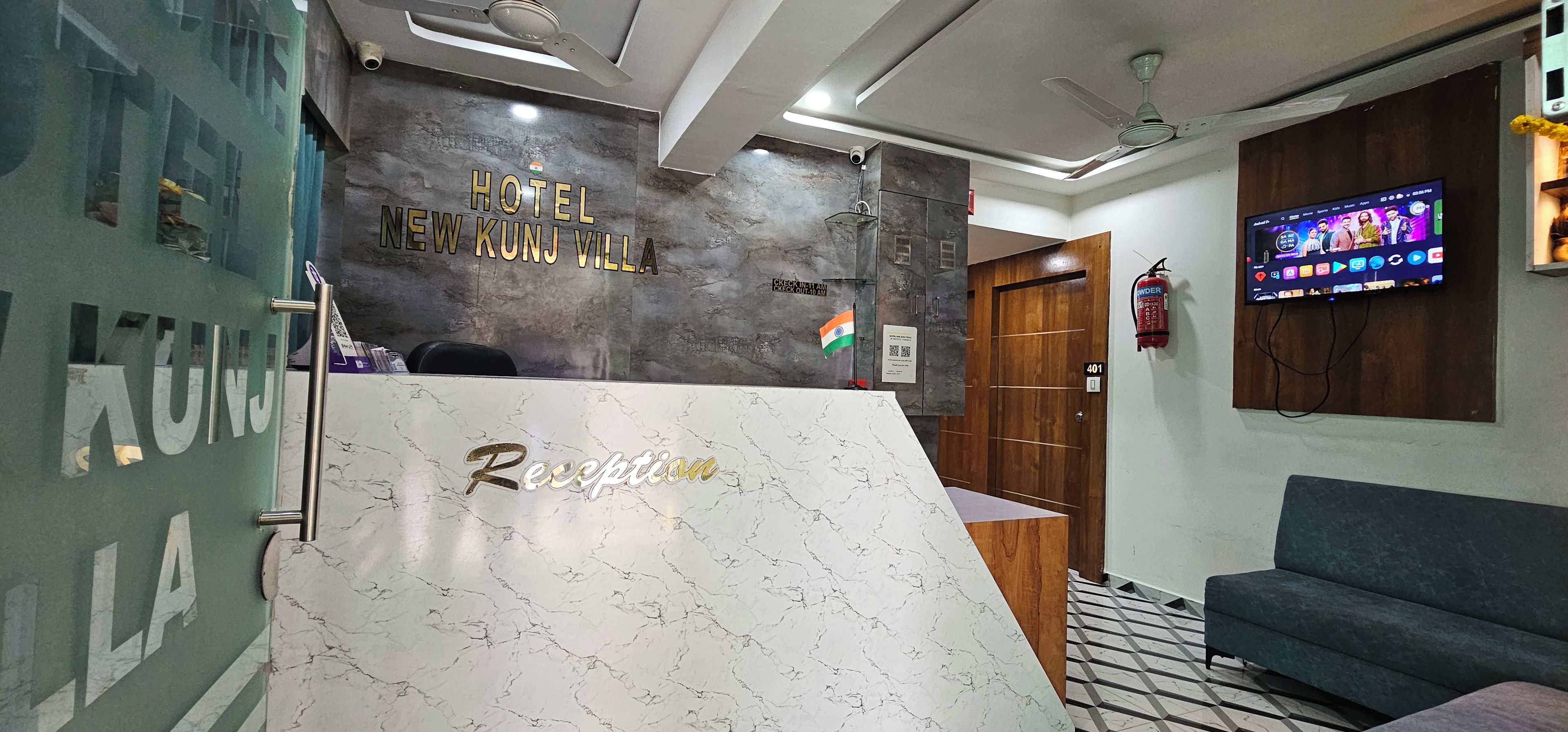 Un comptoir d’accueil surmonté d’un plateau en marbre, avec les mots « Réception » et « Hôtel New Kunj Villa » inscrits sur le mur qui se trouve derrière.