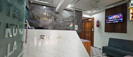 A reception desk with a marble top and the words 'Reception' and 'Hotel New Kunj Villa' on the wall behind it.