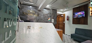 Ein Empfangsschalter mit Marmorplatte und der Aufschrift 'Reception' und 'Hotel New Kunj Villa' an der dahinterliegenden Wand.